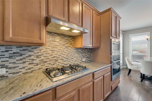 Kitchen featuring under cabinet range hood, decorative backsplash, light stone counters, and appliances with stainless steel finishes | Image 12