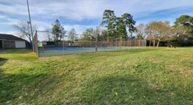 This photo shows a neighborhood tennis court surrounded by a fence, set against a backdrop of trees and a clear sky. | Image 37