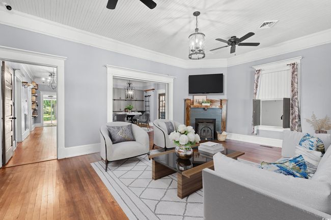 Living room with a chandelier, light wood finished floors, ornamental molding, a fireplace, and ceiling fan | Image 4