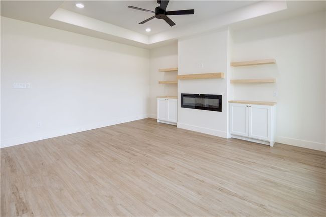 Unfurnished living room with a raised ceiling, a ceiling fan, light wood finished floors, a glass covered fireplace, and recessed lighting | Image 7