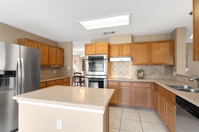 Kitchen with appliances with stainless steel finishes, a sink, decorative backsplash, a center island, and tile floors. | Image 19