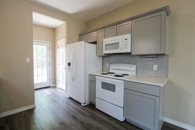 Kitchen featuring gray cabinetry, white appliances, decorative backsplash, and dark wood-style floors | Image 8