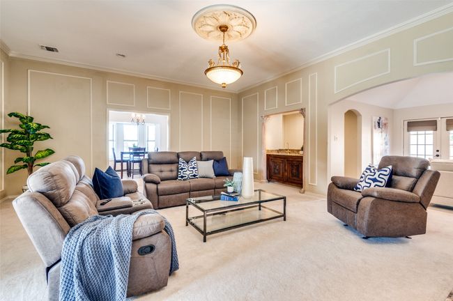 Carpeted living room featuring visible vents, arched walkways, ornamental molding, a chandelier, and a decorative wall | Image 13