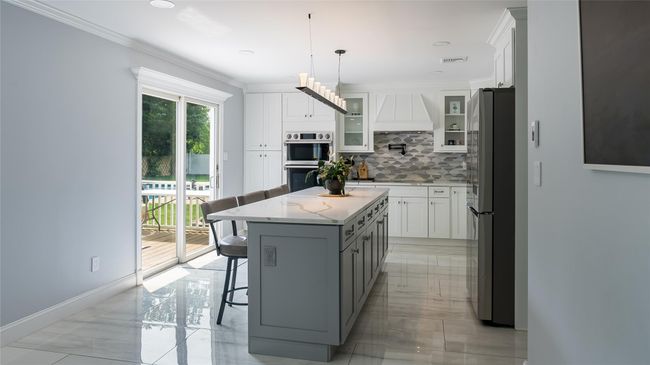 Kitchen with appliances with stainless steel finishes, backsplash, white cabinetry, premium range hood, and light marble finish floors | Image 11