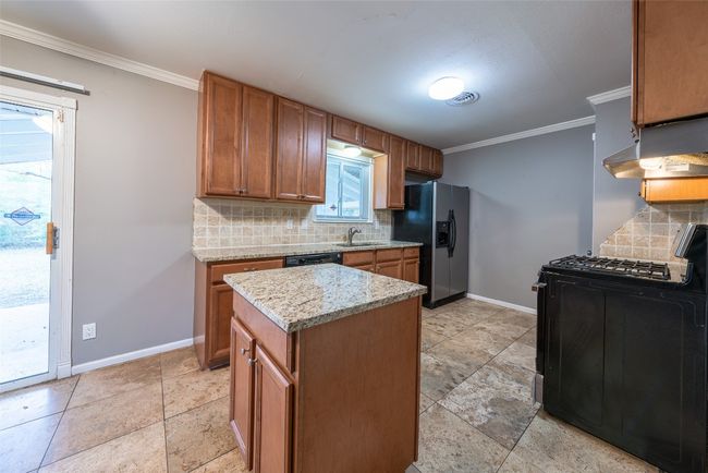 Kitchen featuring black appliances, decorative backsplash, under cabinet range hood, ornamental molding, and brown cabinetry | Image 8