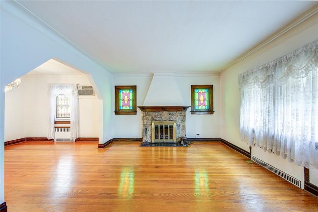 Living area with a stone fireplace, a wall mounted air conditioner, wood finished floors, and ornamental molding | Image 5