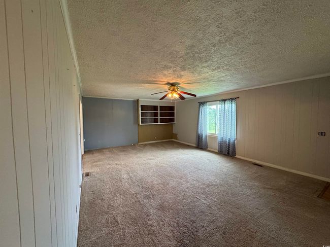Carpeted spare room featuring ceiling fan, a textured ceiling, and wood walls | Image 7