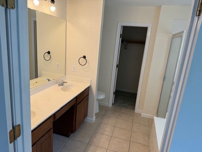 Full bath with double vanity, toilet, a walk in closet, tile patterned floors, and a shower | Image 9