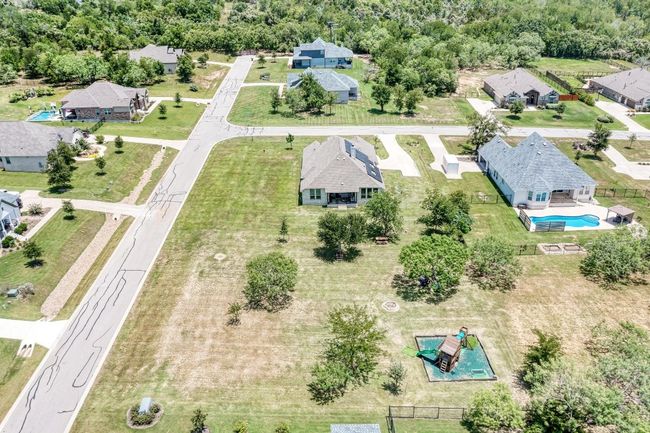 The aerial view from the back of 104 Black Talon's lot, revealing the pretty treed backyard, playscape and firepit. | Image 23