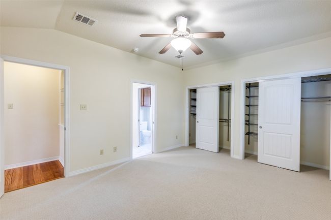 Unfurnished bedroom featuring light carpet, multiple closets, ensuite bath, and a ceiling fan | Image 22