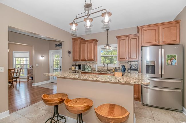 Kitchen featuring stainless steel fridge, light stone counters, hanging light fixtures, and backsplash | Image 10
