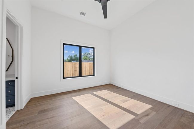 This downstairs secondary bedroom offers privacy and versatility—ideal for guests or multigenerational living. Soft natural light filters through large windows, highlighting the wide-plank oak flooring and serene neutral palette. The ensuite bath continues the refined aesthetic with designer tile, sleek fixtures, and a spacious walk-in shower. | Image 24