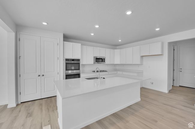 Kitchen featuring stainless steel appliances, white cabinets, light wood-style flooring, light countertops, and recessed lighting | Image 8