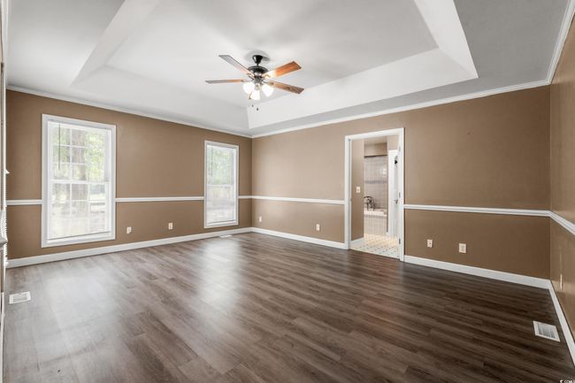Unfurnished room with a tray ceiling, healthy amount of natural light, ceiling fan, dark wood-style flooring, and crown molding | Image 14