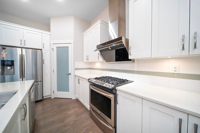Kitchen with stainless steel appliances, wall chimney range hood, tasteful backsplash, and light countertops | Image 14