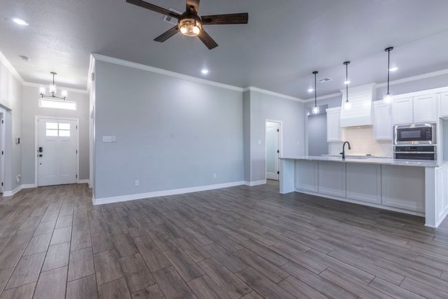 Unfurnished living room with ceiling fan, crown molding, dark wood finished floors, recessed lighting, and a chandelier | Image 5