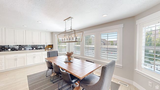 Dining area featuring a textured ceiling, visible vents, light wood finished floors, baseboards, and a notable chandelier | Image 4