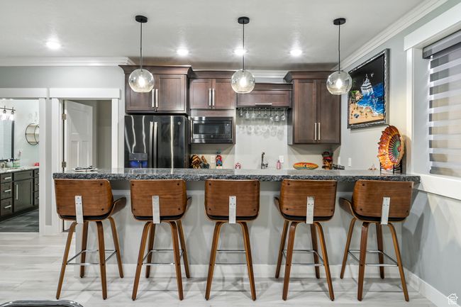 Kitchen featuring stainless steel fridge with ice dispenser, built in microwave, crown molding, dark brown cabinetry, and a kitchen breakfast bar | Image 66