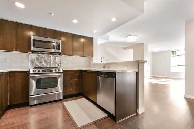 Kitchen featuring appliances with stainless steel finishes, a peninsula, light countertops, dark wood-style floors, and recessed lighting | Image 11