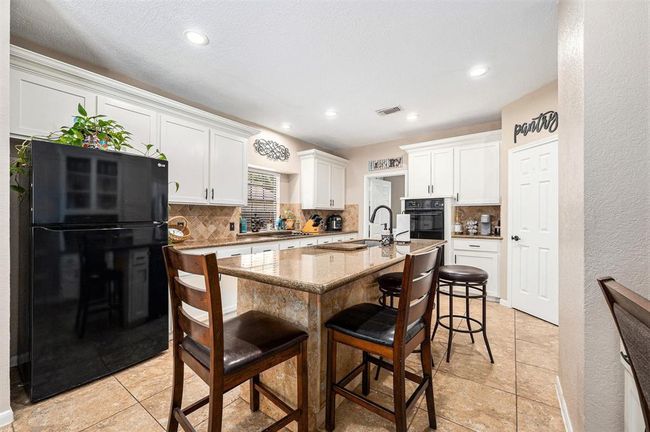 Amazing island kitchen features gorgeous granite countertops, black appliances, tile backsplash, white cabinetry and a built-in desk with a hutch. | Image 8