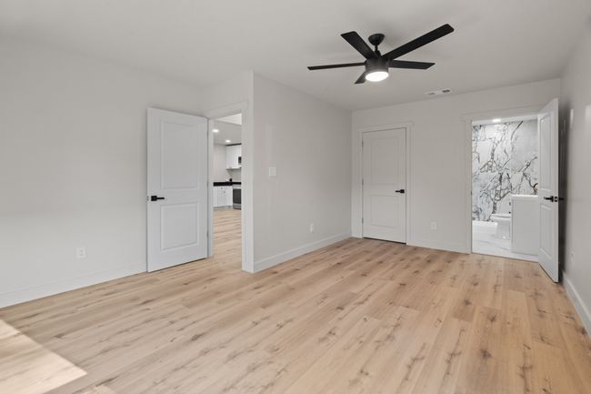 Unfurnished bedroom with light wood finished floors, baseboards, ensuite bath, and ceiling fan | Image 10