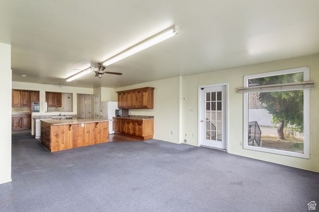 Kitchen with light countertops, a center island, brown cabinets, and dark carpet | Image 10