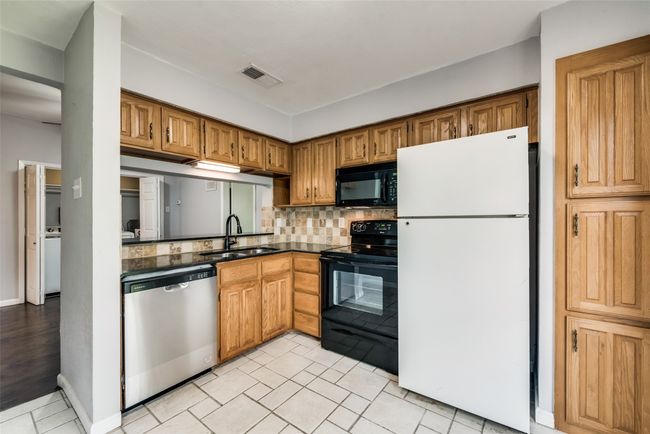 Kitchen with black appliances, dark countertops, decorative backsplash, and brown cabinetry | Image 7