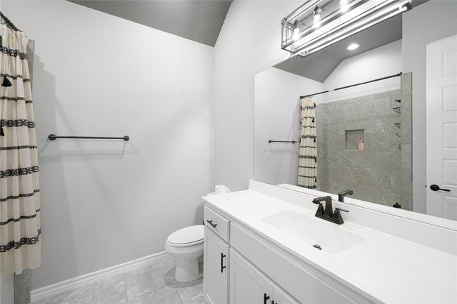 Full bathroom featuring baseboards, toilet, vanity, tiled shower, and vaulted ceiling | Image 19