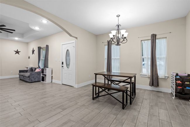Dining area with light wood-style floors, a chandelier, arched walkways, a ceiling fan, and a raised ceiling | Image 17
