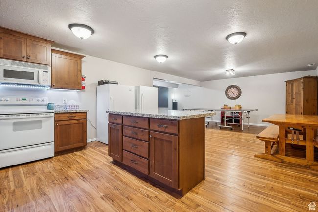 Kitchen featuring light wood-style flooring, a textured ceiling, brown cabinetry, and white appliances | Image 47