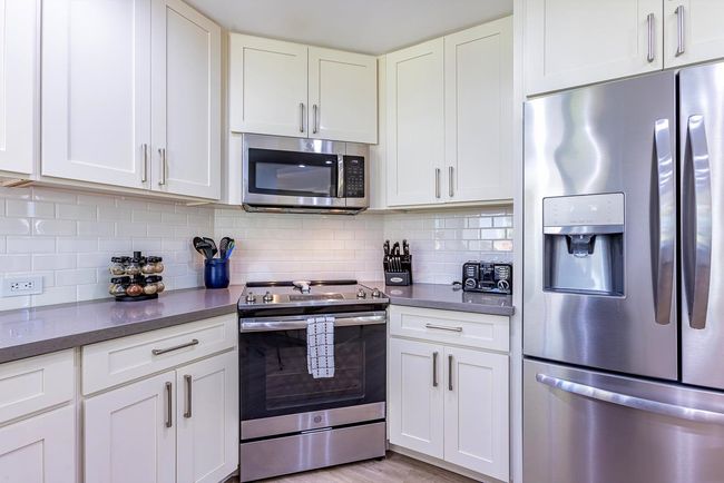 The fully-equipped kitchen boasts newer stainless steel appliances & a custom full-height backsplash | Image 9