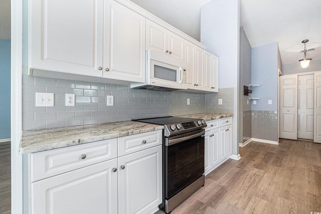 Kitchen with stainless steel electric stove, light wood-style floors, white microwave, white cabinetry, and light stone countertops | Image 16