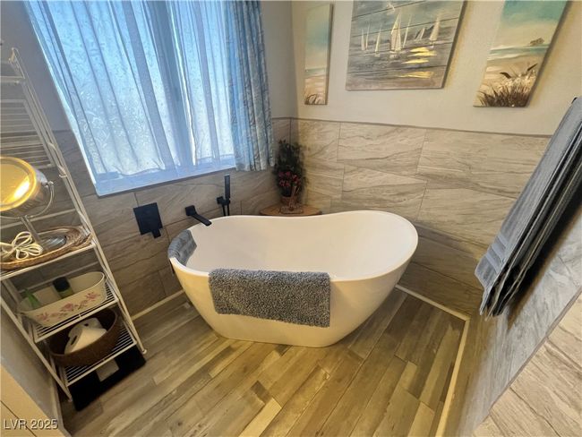 Full bath with wood finished floors, tile walls, a soaking tub, and wainscoting | Image 43