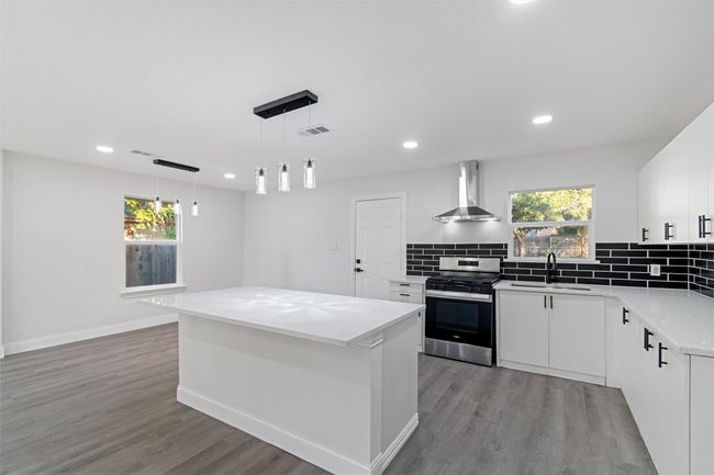 Kitchen featuring plenty of natural light, wall chimney range hood, stainless steel range, and white cabinets | Image 15