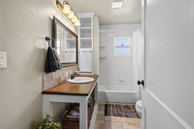 Bathroom with shower / bathtub combination with curtain, toilet, tile patterned flooring, vanity, and a textured wall | Image 4