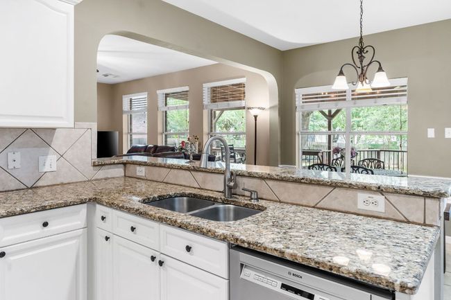 Kitchen featuring a sink, arched walkways, a chandelier, dishwashing machine, and light stone countertops | Image 12