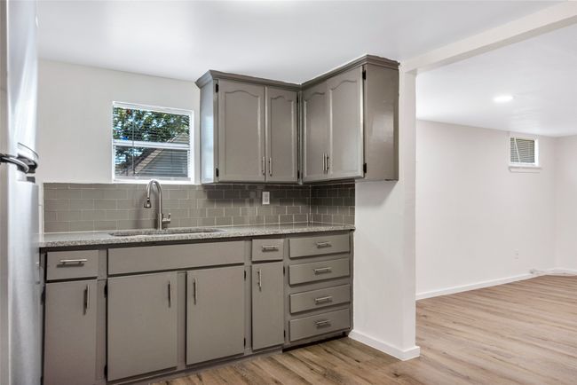 Kitchen with gray cabinets, light wood-style flooring, decorative backsplash, and light stone countertops | Image 28