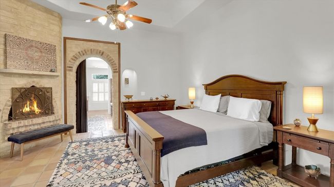 Bedroom with arched walkways, a towering ceiling, a ceiling fan, a fireplace, and light tile patterned floors | Image 23