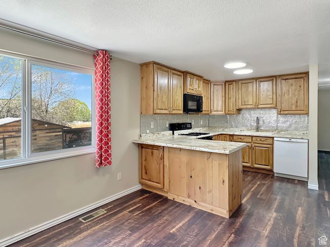 Kitchen featuring black microwave, dishwasher, a sink, range with gas stovetop, and dark wood-type flooring | Image 9
