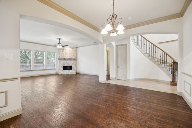 Unfurnished living room with ceiling fan, wood finished floors, a fireplace, ornamental molding, and a chandelier | Image 11