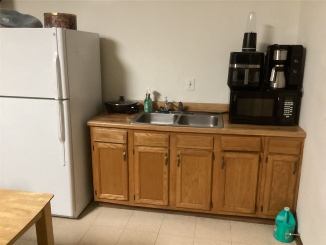 Kitchen featuring a sink, freestanding refrigerator, light tile patterned flooring, brown cabinetry, and black microwave | Image 19