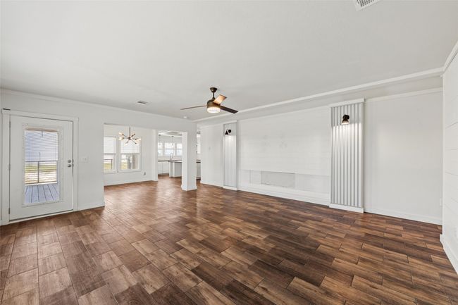Unfurnished living room with a chandelier, dark wood finished floors, ceiling fan, crown molding, and arched walkways | Image 5