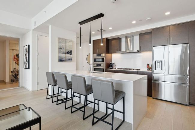 Kitchen featuring appliances with stainless steel finishes, wall chimney exhaust hood, light wood-style flooring, dark brown cabinets, and light countertops | Image 17