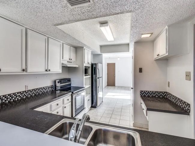 Kitchen with appliances with stainless steel finishes, under cabinet range hood, dark countertops, light tile patterned flooring, and white cabinets | Image 9