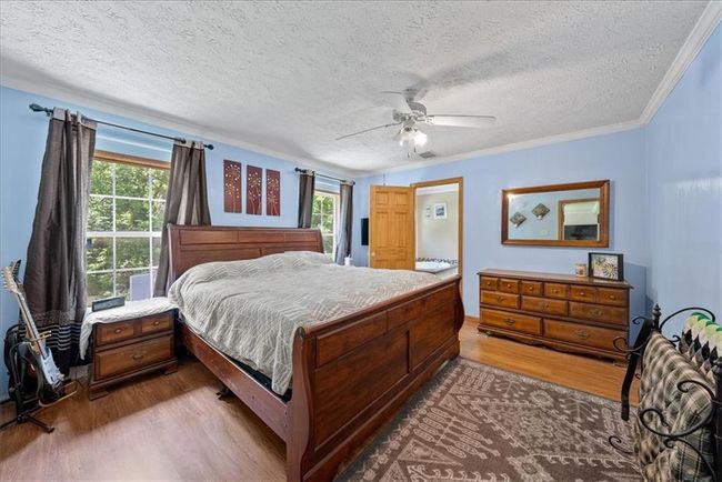 Bedroom with dark wood-style floors, crown molding, a ceiling fan, and a textured ceiling | Image 23