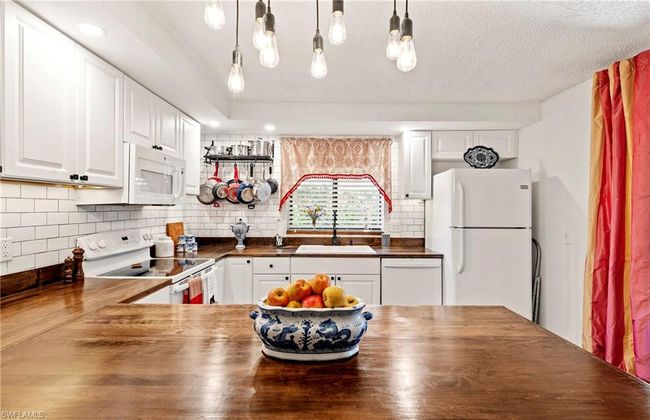 Kitchen with butcher block counters, white appliances, white cabinetry, tasteful backsplash, and hanging light fixtures | Image 12