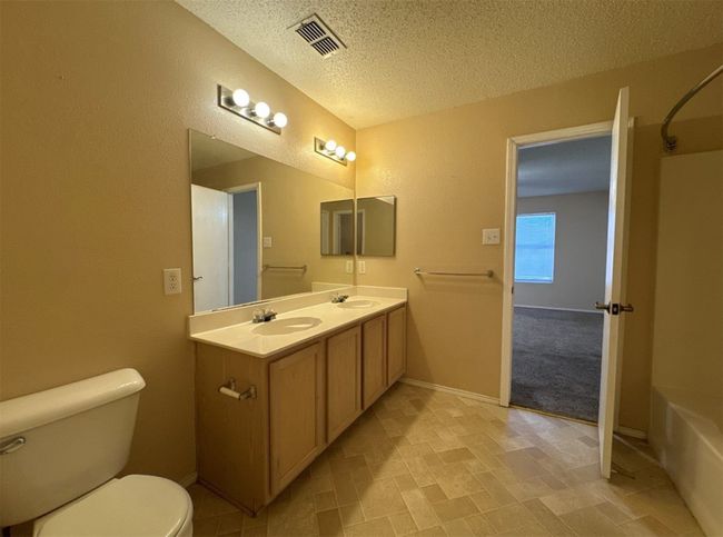Full bathroom featuring vanity with extensive cabinet space, double sink, tile flooring, toilet, and a textured ceiling | Image 24