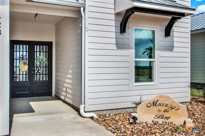 This welcoming entryway features a modern front door with glass elements set in a clean-lined exterior with light siding. A personalized decorative stone adds a charming touch to the landscaping. | Image 2