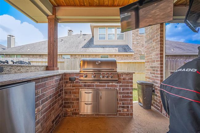 From casual cookouts to festive evenings, this outdoor kitchen offers bar seating, granite countertops, and a warm brick surround for a welcoming vibe. | Image 38