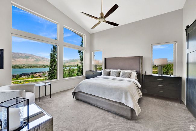 Bedroom with carpet flooring, baseboards, high vaulted ceiling, a barn door, and ceiling fan | Image 30